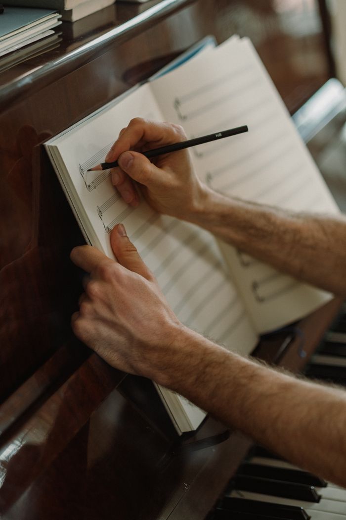 about-02 A person composing music with pencil and sheet on a piano. Captures artistic creativity.