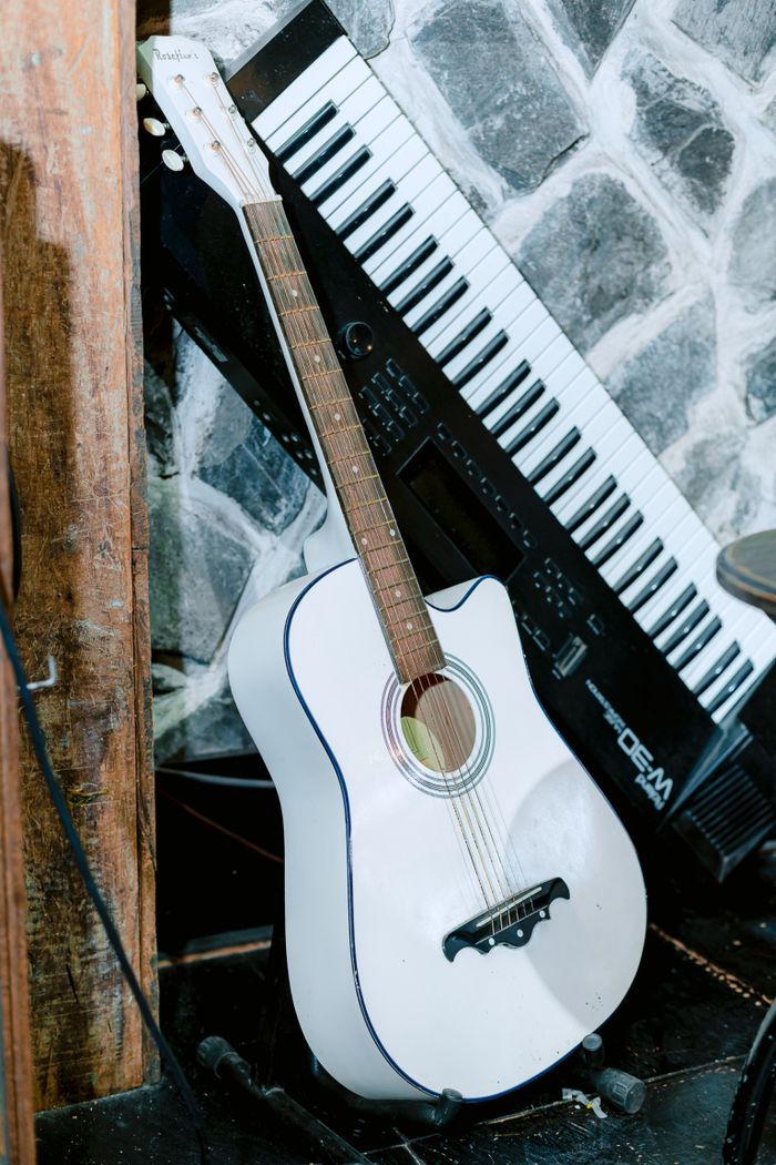 ours-journey A white acoustic guitar leaning against a keyboard on a stone background, exuding a musical ambiance.